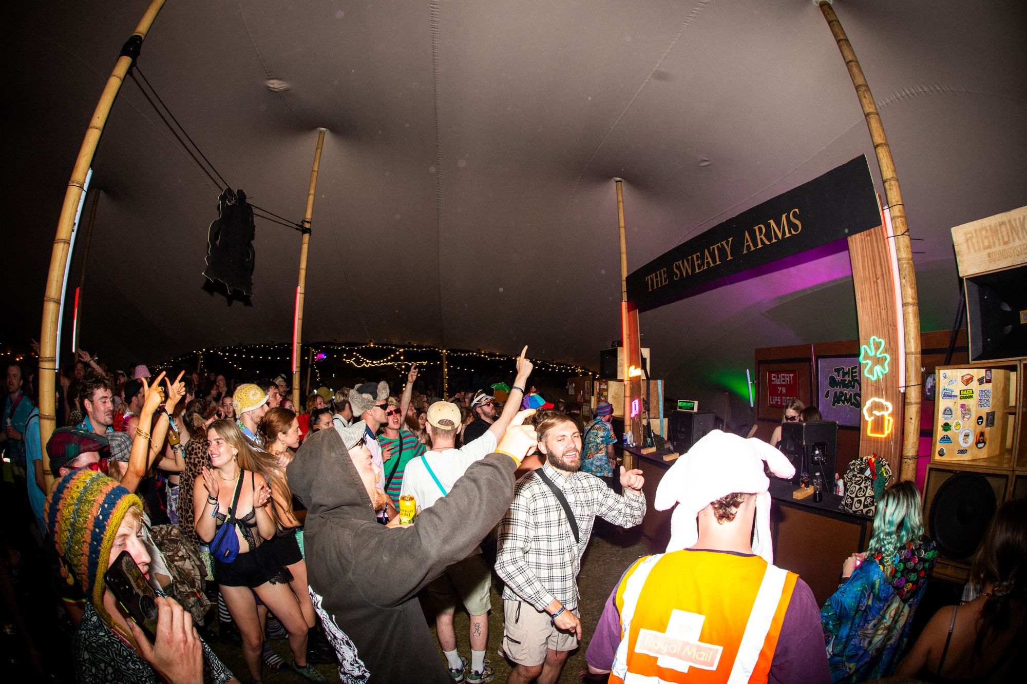 Crowd dancing under the Sweaty Arms sign at night