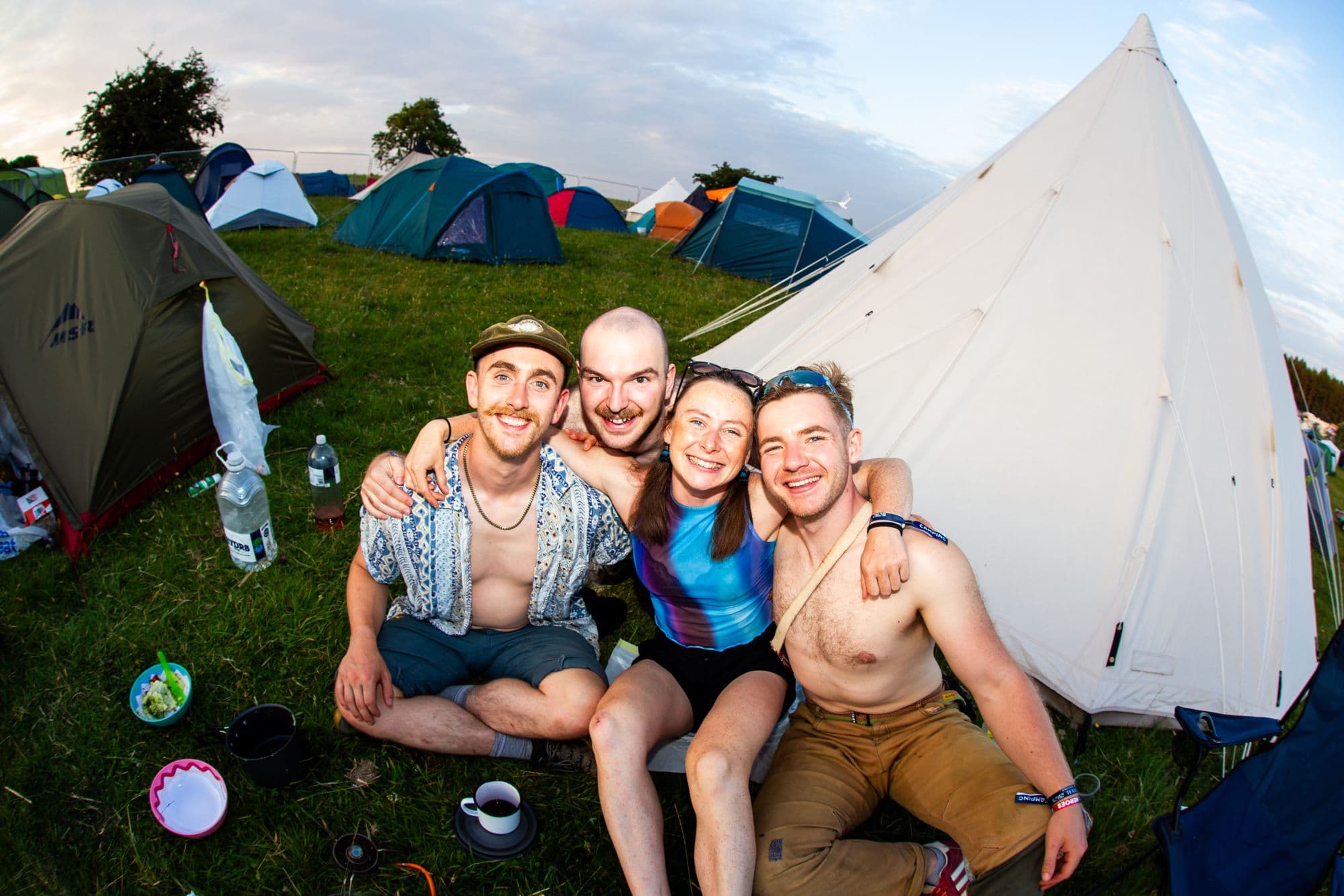 Four happy friends at the campsite in front of their tents